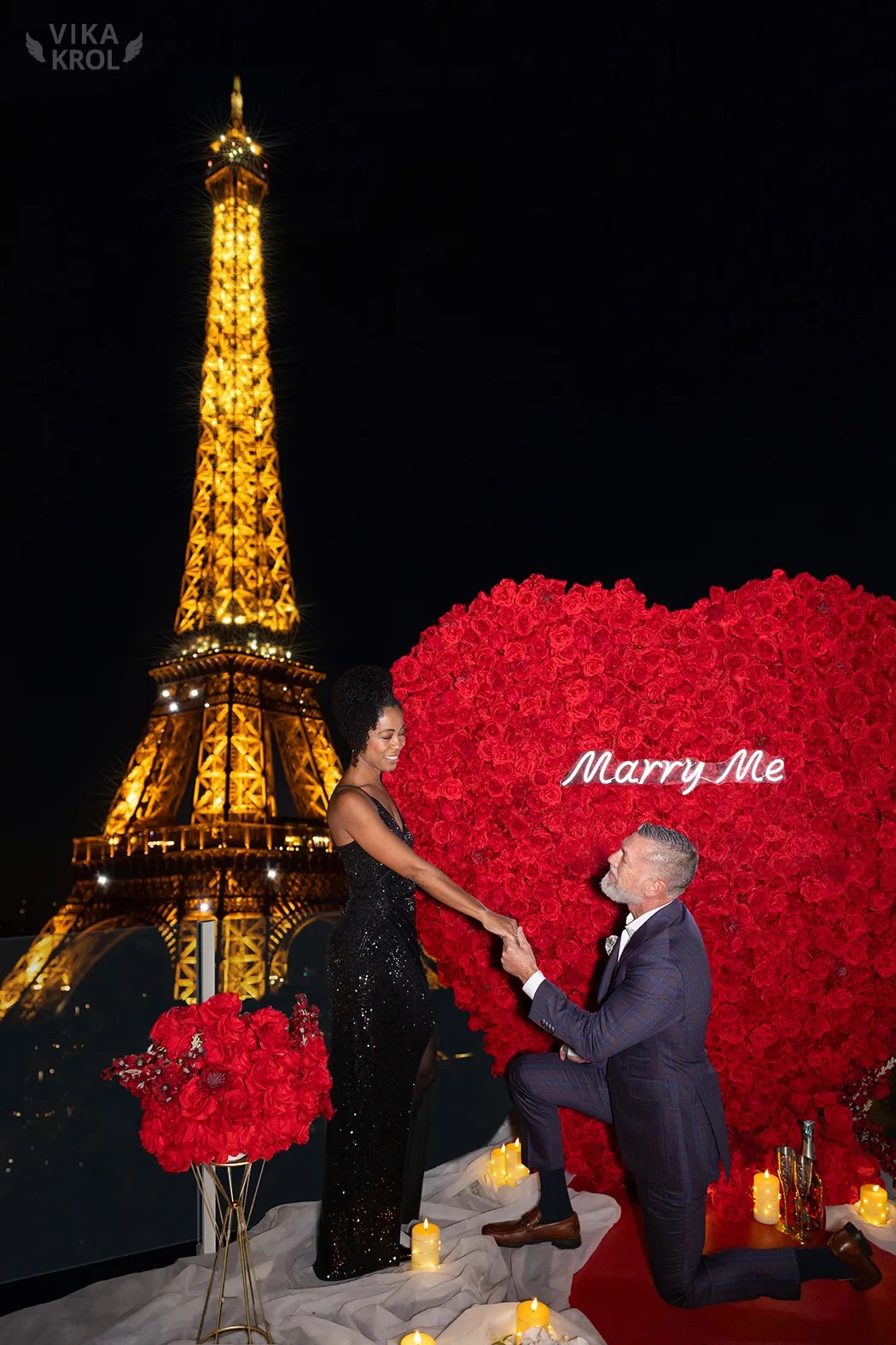 A wide-angle shot of a private Parisian terrace with a red carpet leading toward the Eiffel Tower at night, glowing against a dark blue sky.