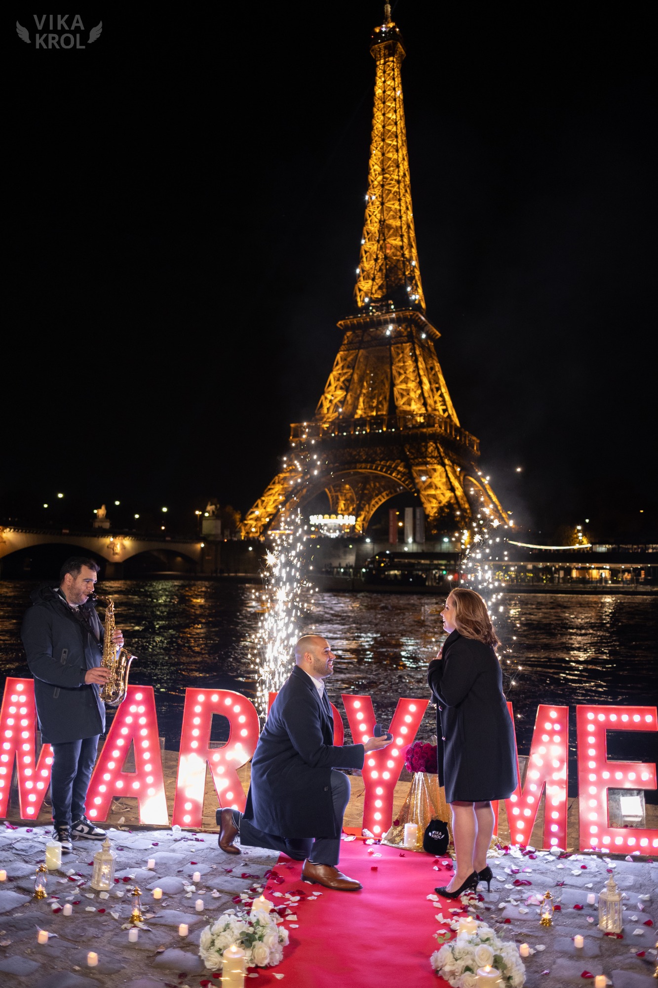 Un coordinateur discret parle à un guest à l'écart, avec la Tour Eiffel floue en arrière-plan. L'ambiance est sérieuse mais rassurante.