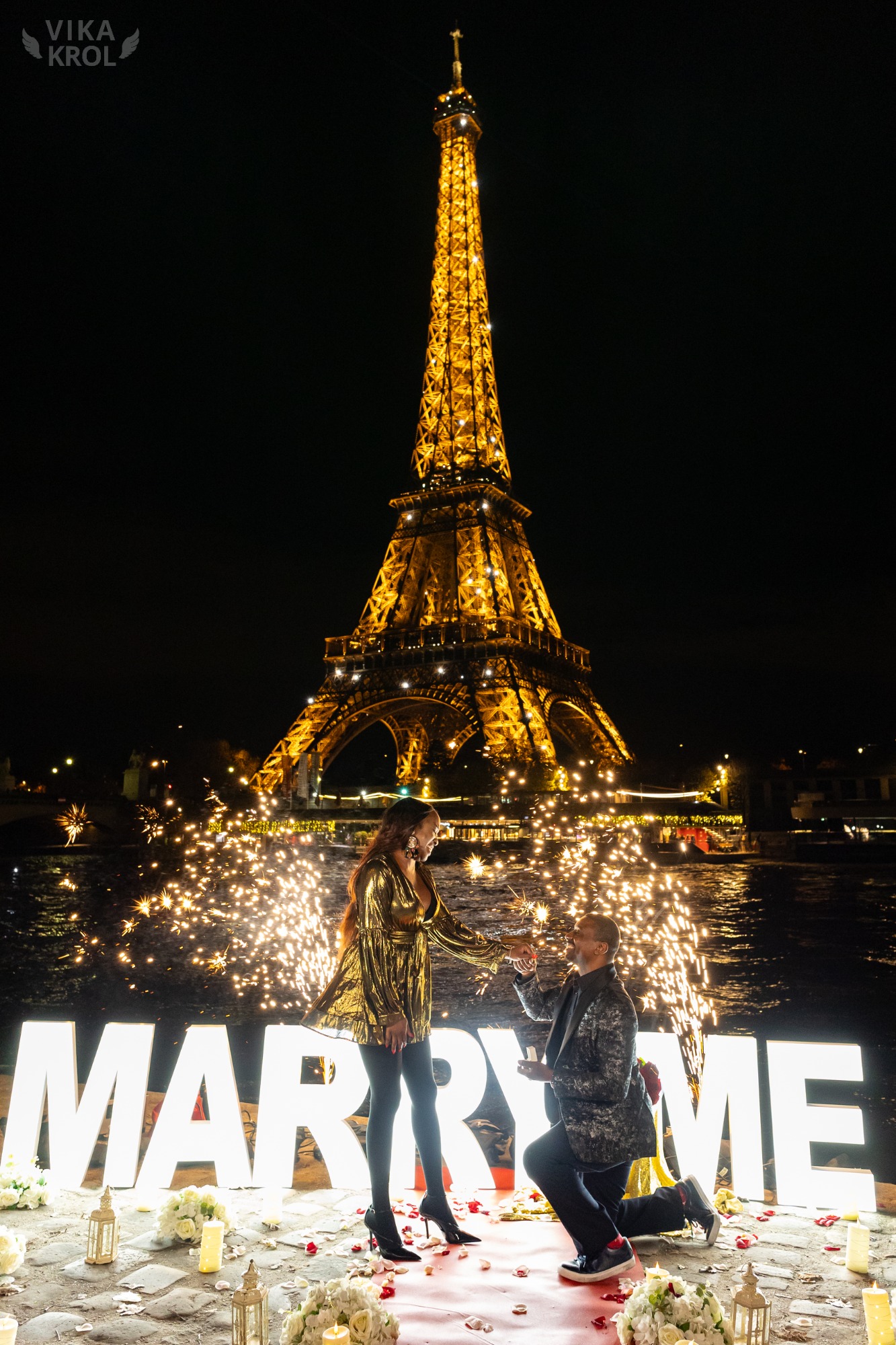 A wide-angle shot of a couple proposing at night, the Eiffel Tower sparkling in the background with a cinematic golden glow and professional night lighting.