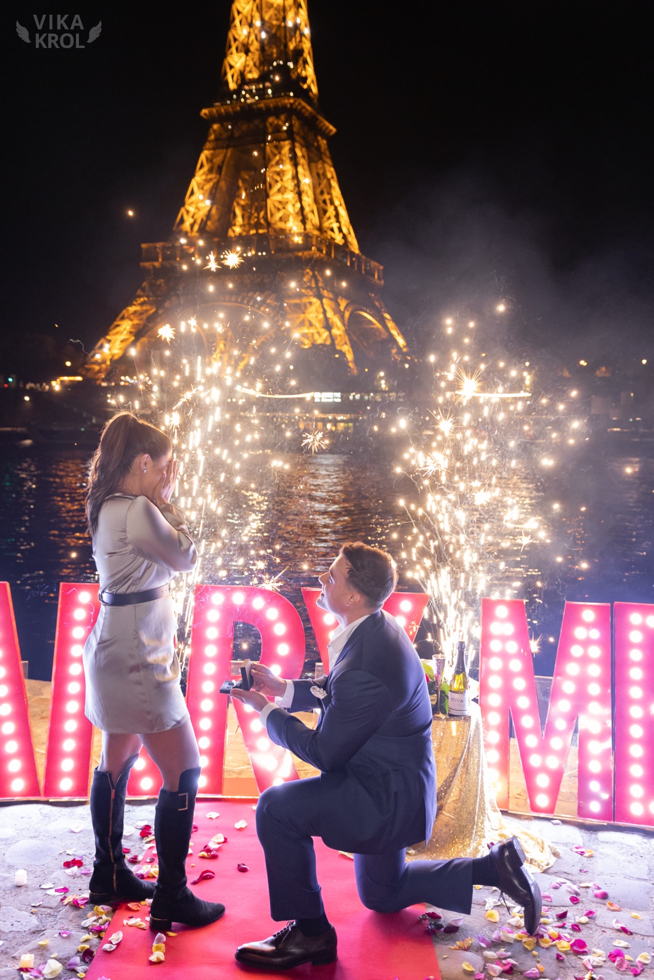 A close-up shot of a couple's hands with the ring, with the crowds of Paris softly blurred into glowing lights in the background.