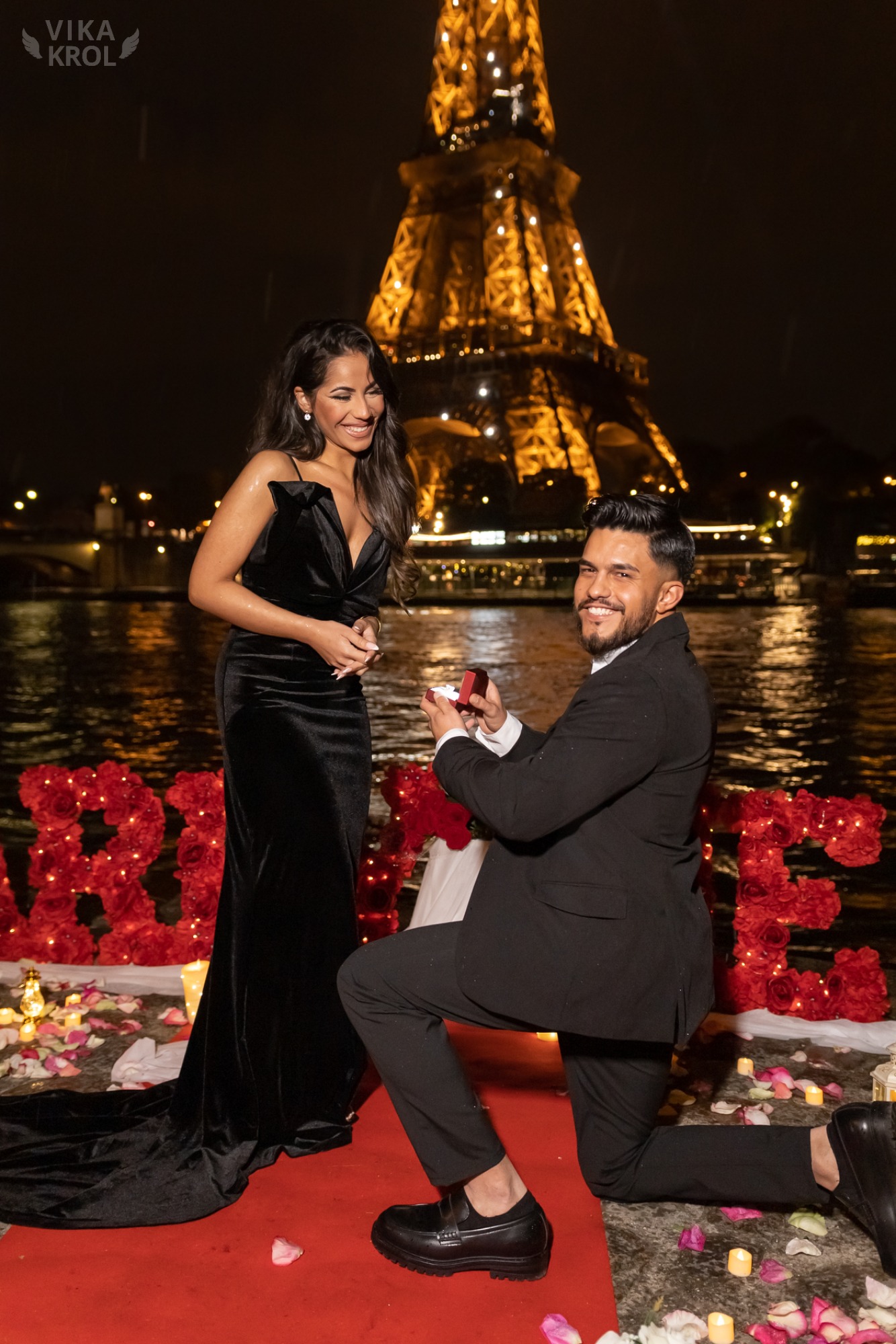 A breathtaking view from a private Parisian rooftop at sunset, with a red carpet, rose petals, and the Eiffel Tower glowing in the distance.